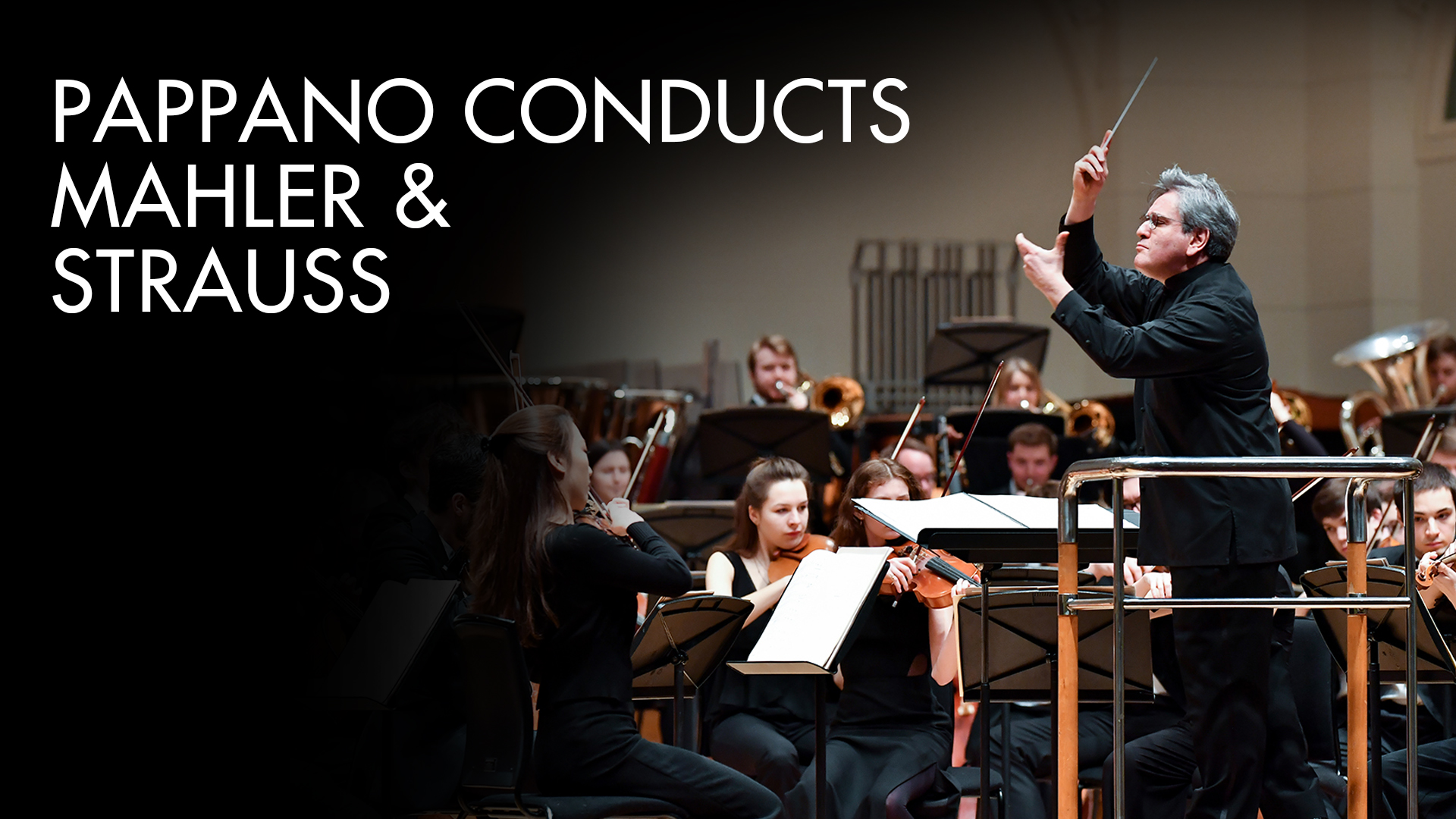 Pappano Conducts Mahler and Strauss A man wearing a black coat, holding a conducting baton, conducting an orchestra of young men and women, wearing smart black attire, performing on musical instruments.